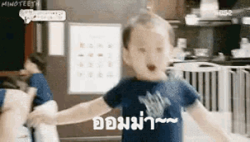 a baby in a blue shirt is holding someone 's hand and has a foreign language written on his shirt