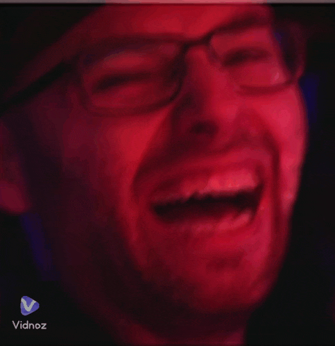 a man with glasses and a beard is laughing in a red background