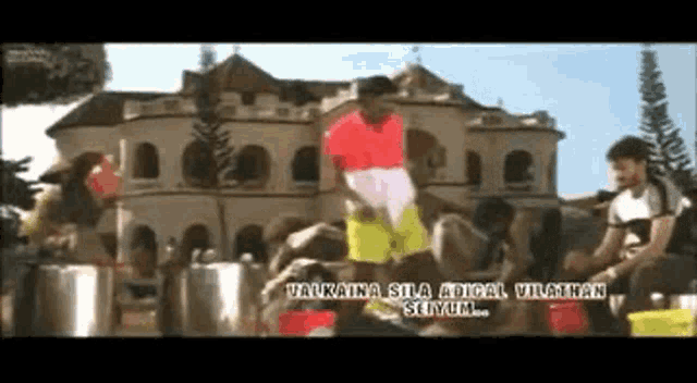 a man in a red shirt is standing in front of a building with the words " valkaina sila adical vivathan selvum "