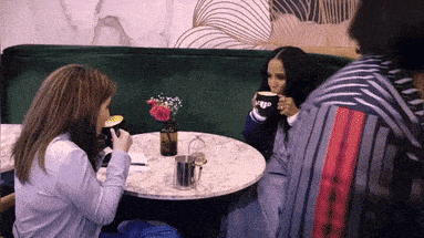 a woman sitting at a table drinking a cup of coffee from a mug that says ' ego ' on it