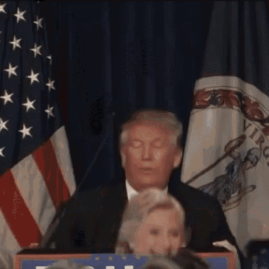 a man and a woman are sitting at a podium in front of a flag .