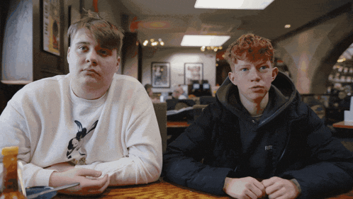 two boys sit at a table with one wearing a black jacket that says boss