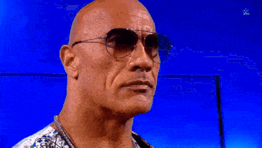 a bald man wearing sunglasses is standing in front of a blue screen .