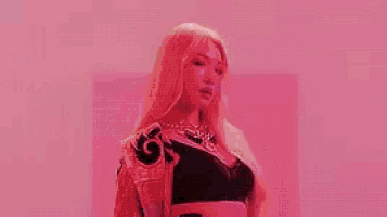 a woman with long blonde hair is wearing a pink jacket and a black top .