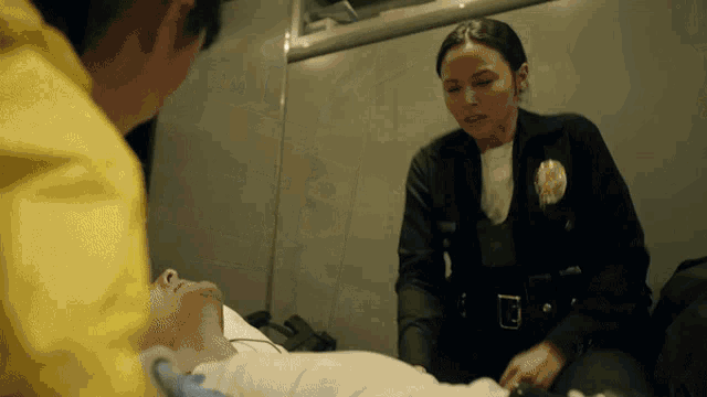 a woman in a police uniform is talking to a man laying on a stretcher