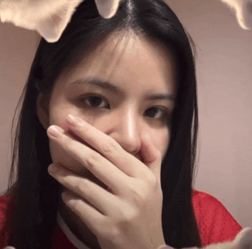 a woman covering her mouth with her hand and a cat behind her head
