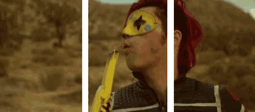 a man with red hair and a yellow mask on his face blowing a balloon