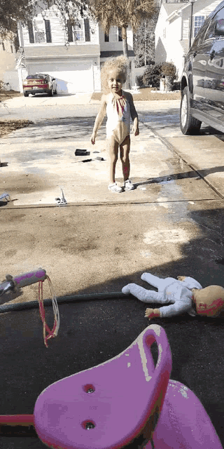 a little girl in a bathing suit is standing next to a pink bicycle