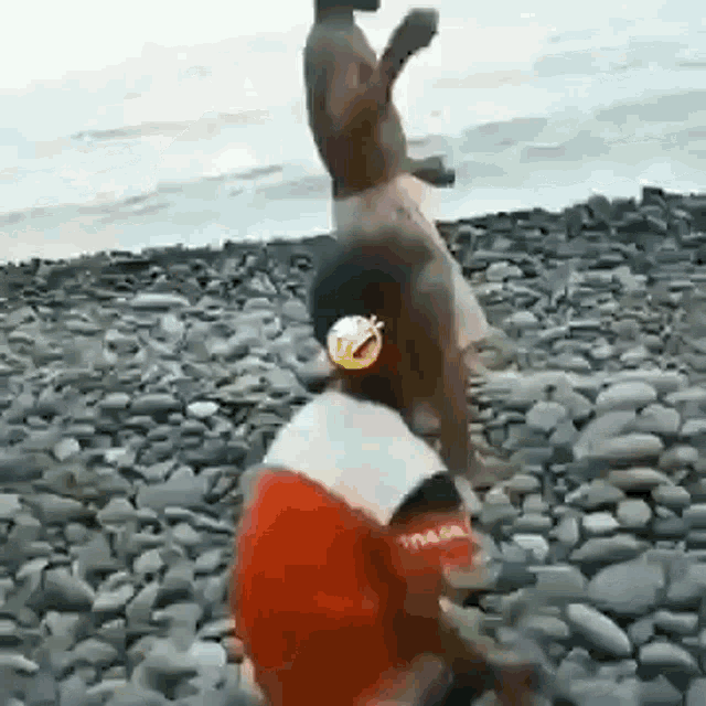 a man is standing on a rocky beach next to a woman in a red shirt .