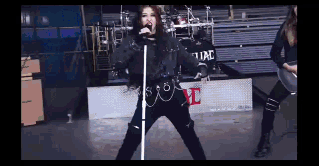a woman is singing into a microphone while standing in front of a drum set in a dark room .