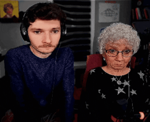 a man wearing headphones stands next to an elderly woman wearing glasses