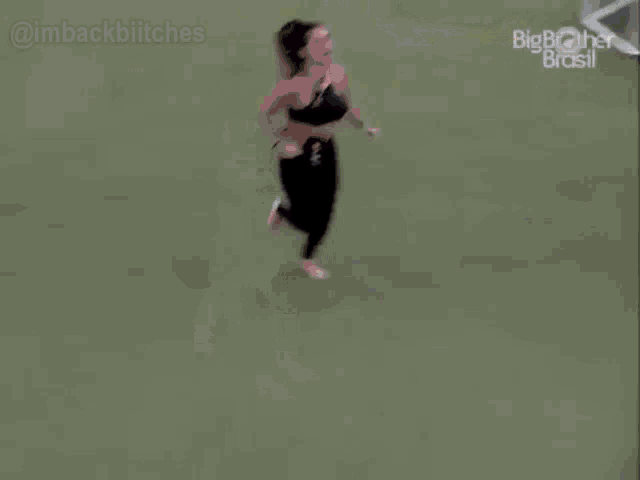 a woman in a black top and black pants is running on a green field .