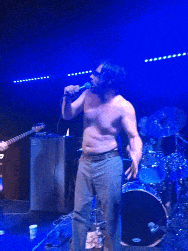 a shirtless man is singing into a microphone on a stage