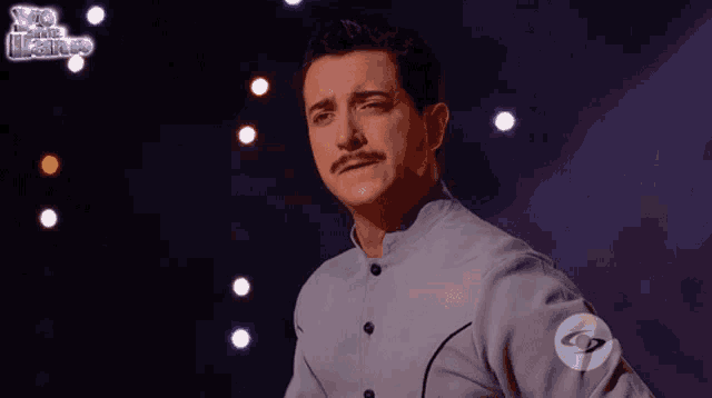 a man with a mustache stands on a stage in front of a sign that says yo soy el maestro