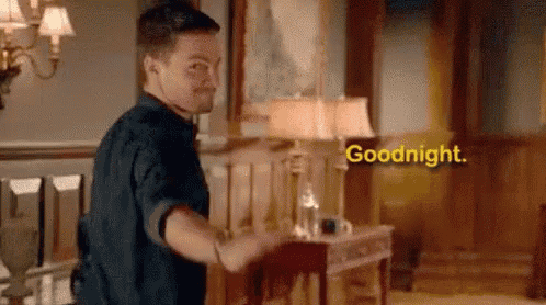 a man is standing in a living room with a lamp and a table and says `` goodnight '' .