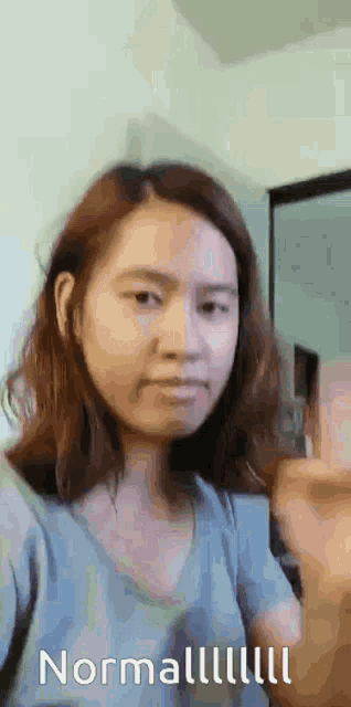 a woman in a blue shirt is taking a selfie with the words normal written below her .