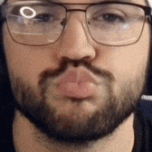 a man with a beard and glasses is blowing a kiss at the camera .