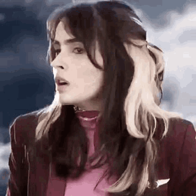 a close up of a woman with long hair wearing a red jacket and a pink shirt .
