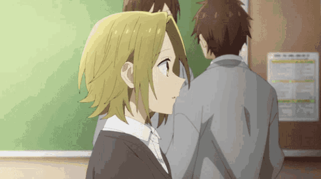 a girl with blonde hair is standing next to a man in a classroom