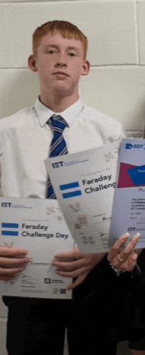 a boy in a white shirt and blue tie is holding a faraday challenge day certificate