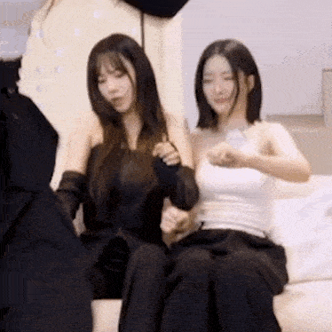 two women are sitting next to each other on a couch and holding hands .