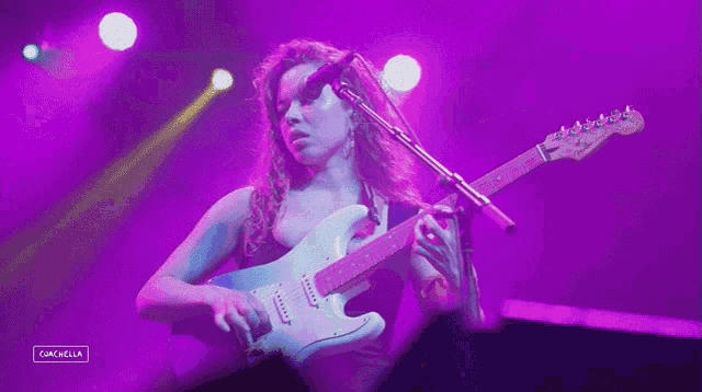 a woman is playing a guitar and singing into a microphone with purple lights behind her and the word cancela on the bottom right