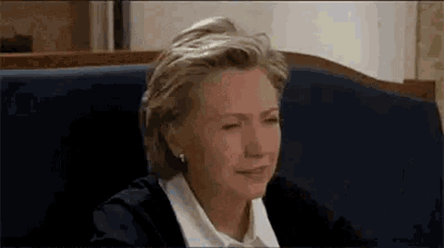 hillary clinton is sitting on a blue couch with her eyes closed .