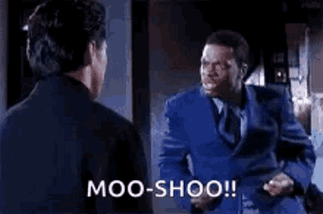 a man in a blue suit and tie is talking to another man in a black shirt .
