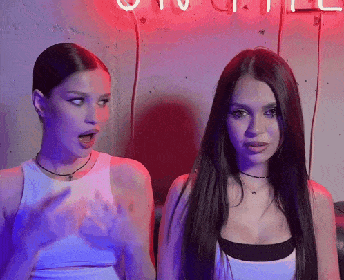 two women are standing next to each other in front of a neon sign that says ' otv ' on it