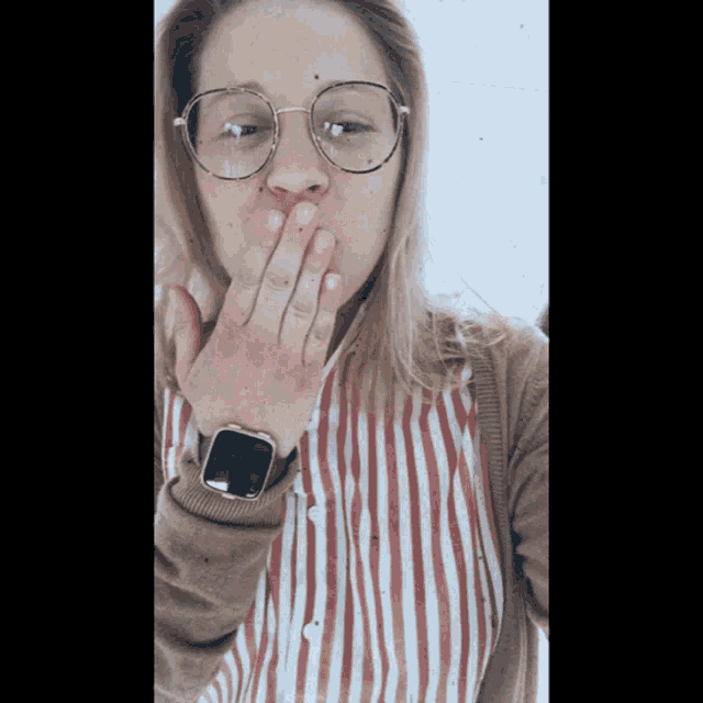 a woman wearing glasses and a watch covers her mouth with her hand
