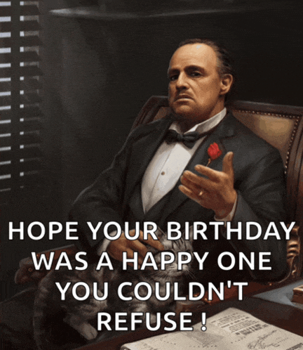 a man in a tuxedo is sitting at a table with a cat and a rose in his hand