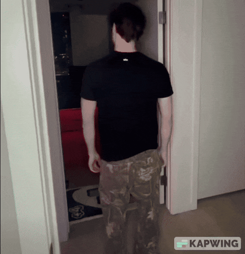 a man in a black shirt and khaki pants stands in a doorway with kapwing written on the bottom right
