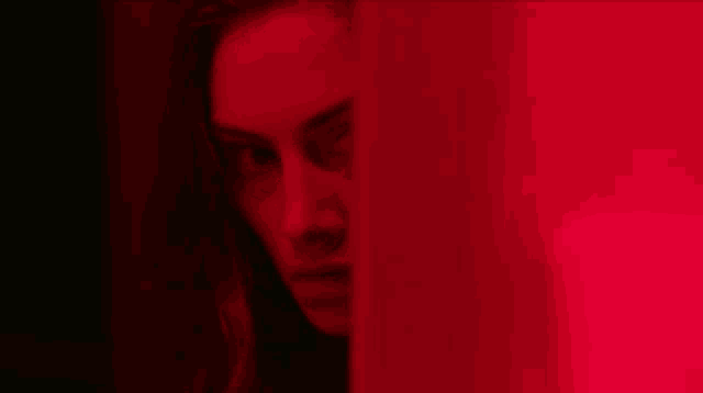 a woman 's face is visible through a red curtain .