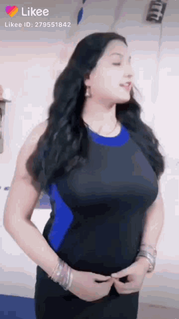 a woman in a black and blue dress is standing in front of a white wall and smiling .