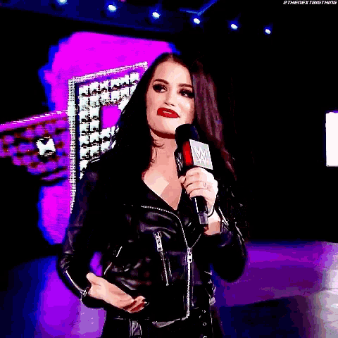 a woman in a leather jacket is holding a microphone in front of a raw sign .