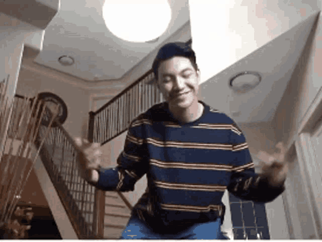 a man wearing a striped shirt is dancing in a room with stairs