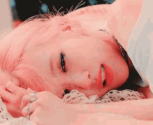a woman with pink hair is laying on her stomach on a bed with her eyes closed .