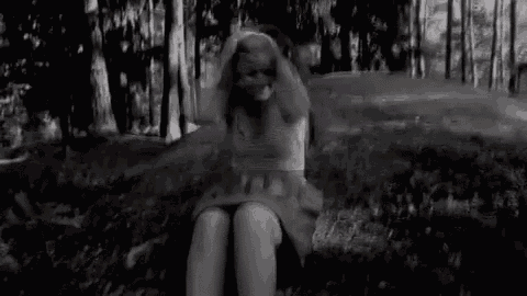 a black and white photo of a woman sitting on a rock in the woods .