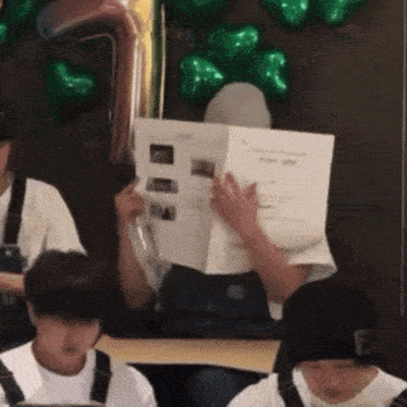 a group of people are sitting in front of a wall with green balloons