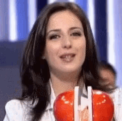 a woman is holding two red apples with straws in her mouth .