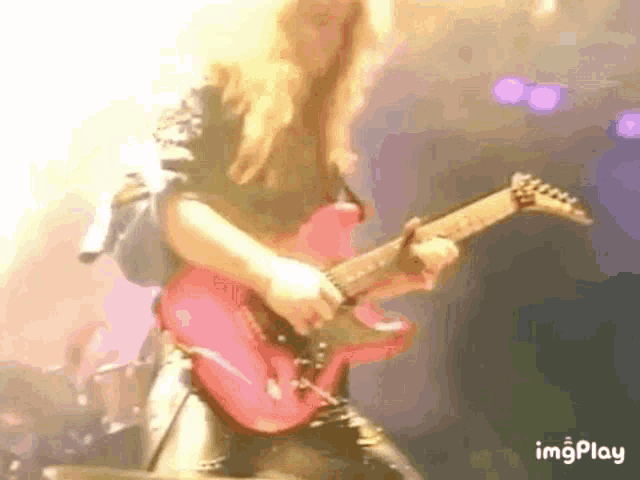 a person is playing a pink electric guitar on stage .