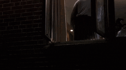 a person is standing in a dark room looking out of a window .