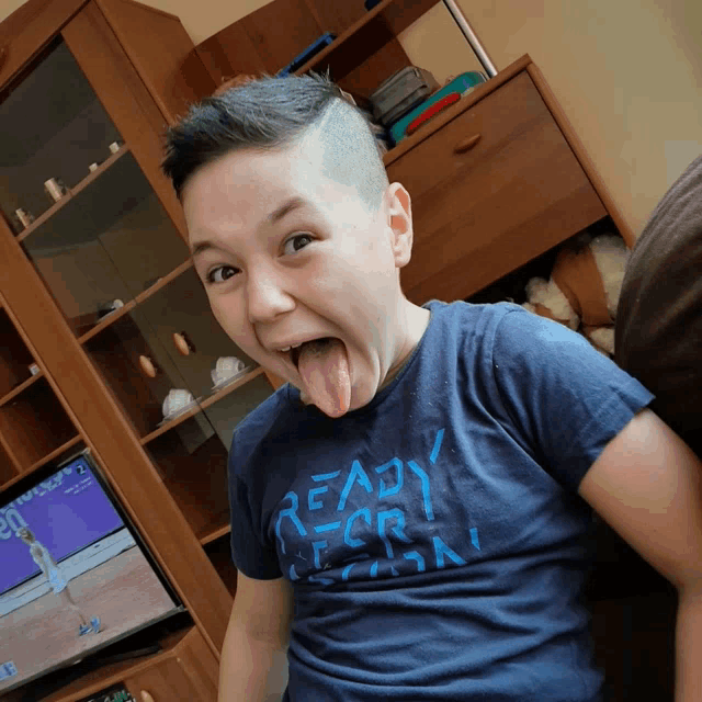 a young boy wearing a blue shirt that says ready for action sticking his tongue out