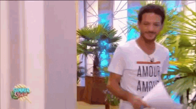 a man wearing a t-shirt that says amour is standing in front of palm trees .