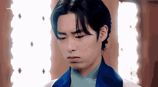a young man wearing a blue jacket and a white shirt is making a sad face .