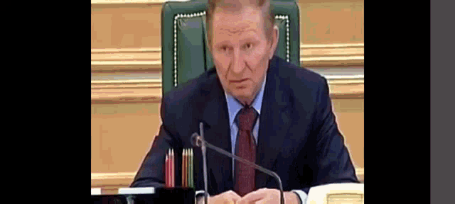a man in a suit and tie is sitting at a table with a microphone .
