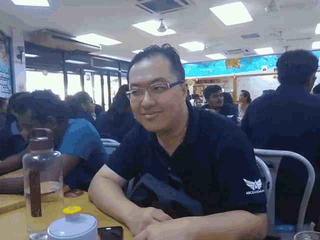 a man wearing a michigan shirt sits at a table with other people
