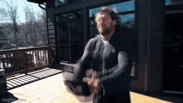 a man with a beard is standing on a deck holding a helmet ..