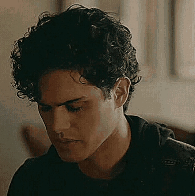 a close up of a man 's face with curly hair and a black shirt .