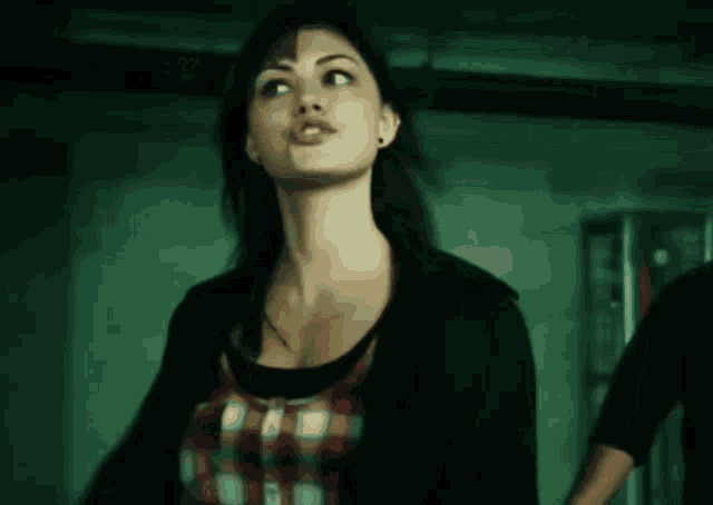 a woman wearing a plaid shirt and a black jacket looks to the side